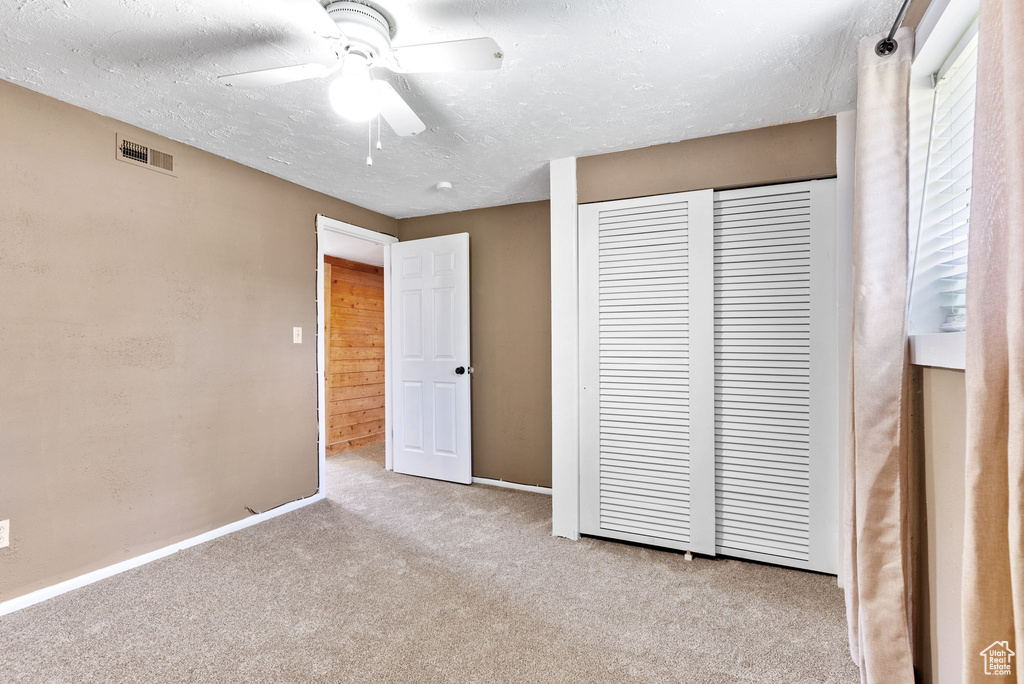 Unfurnished bedroom with a textured ceiling, a closet, carpet floors, and ceiling fan