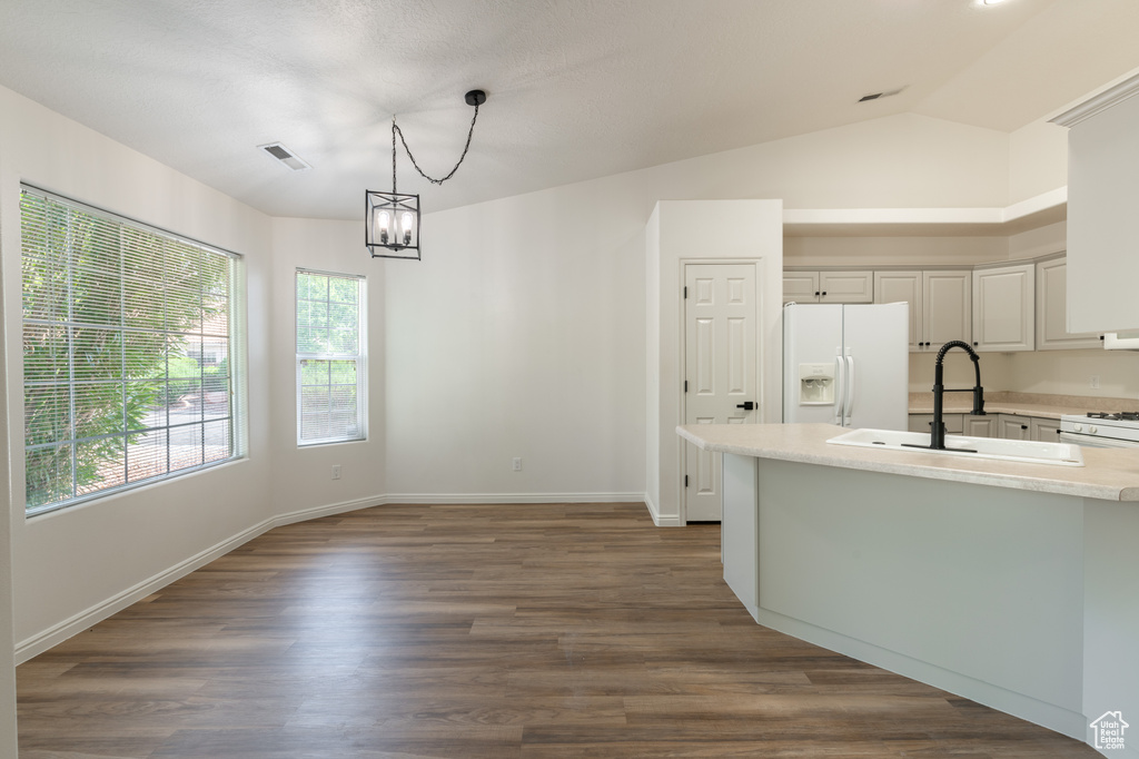 Kitchen with white appliances, vaulted ceiling, hanging light fixtures, dark hardwood / wood-style floors, and a chandelier