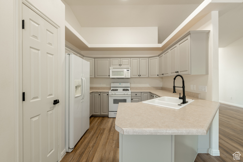 Kitchen featuring wood-type flooring, a tray ceiling, white appliances, sink, and kitchen peninsula