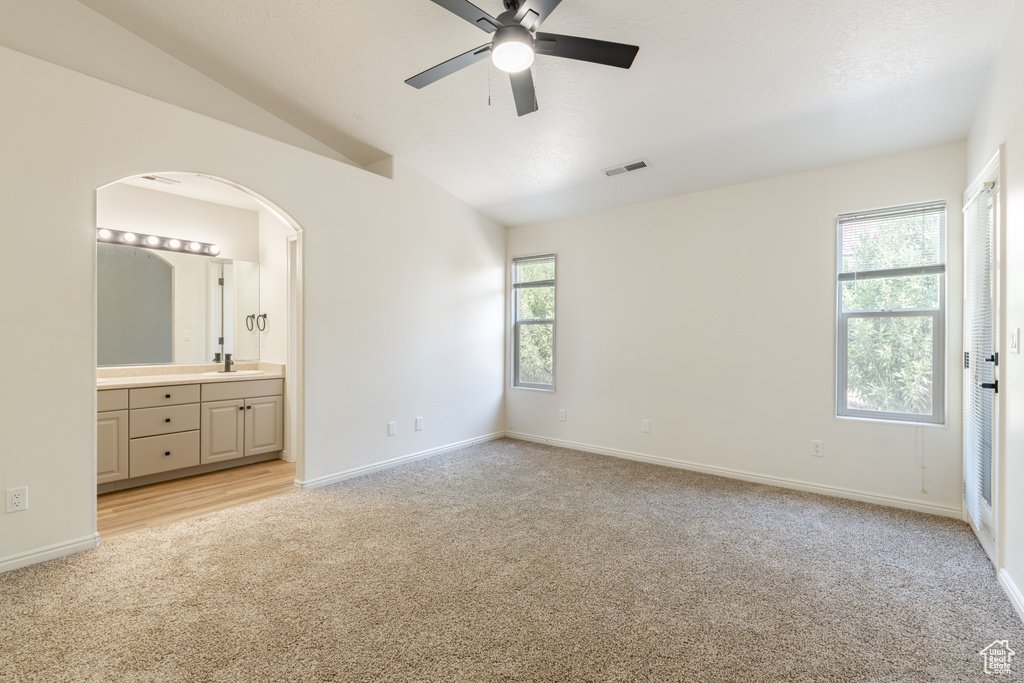 Unfurnished bedroom with lofted ceiling, light carpet, multiple windows, and ensuite bathroom