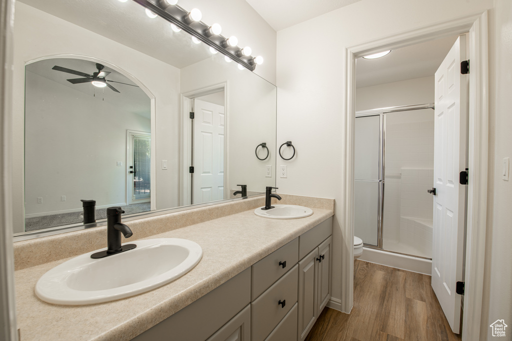 Bathroom with ceiling fan, hardwood / wood-style floors, an enclosed shower, dual bowl vanity, and toilet