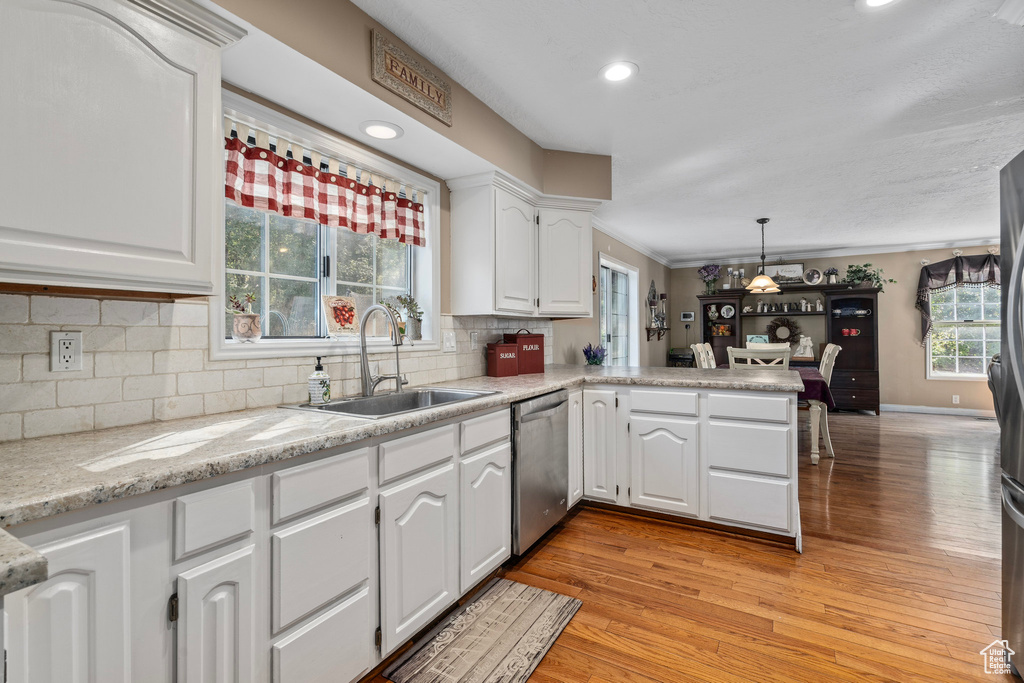 Kitchen with light hardwood / wood-style flooring, pendant lighting, white cabinetry, dishwasher, and sink