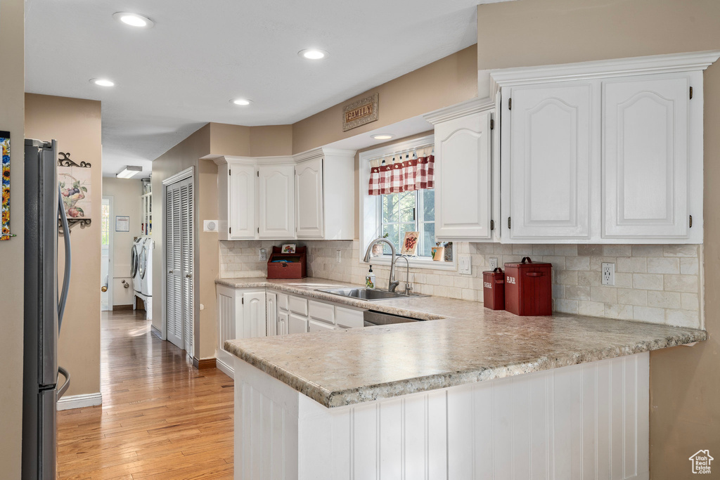 Kitchen with light hardwood / wood-style floors, decorative backsplash, white cabinetry, stainless steel refrigerator, and kitchen peninsula