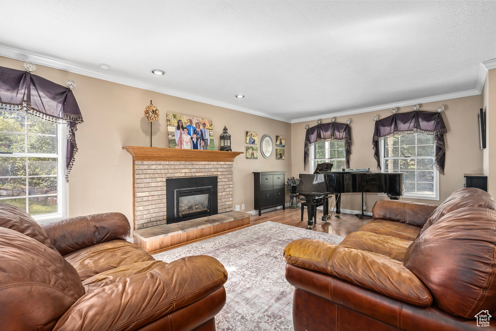 Living room featuring a wealth of natural light, light hardwood / wood-style flooring, a brick fireplace, and ornamental molding