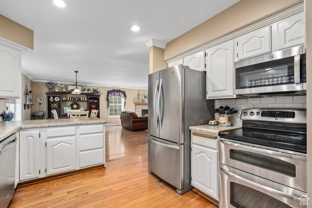 Kitchen featuring appliances with stainless steel finishes, decorative light fixtures, light hardwood / wood-style floors, decorative backsplash, and white cabinetry