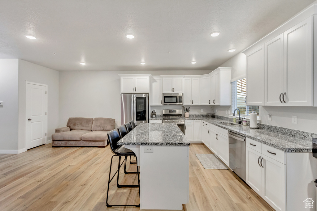 Kitchen with stone counters, light wood-type flooring, sink, a center island, and appliances with stainless steel finishes