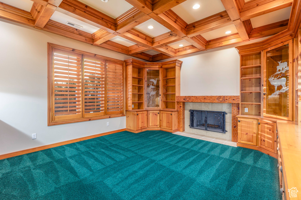 Unfurnished living room featuring a tile fireplace, built in shelves, light carpet, coffered ceiling, and beam ceiling