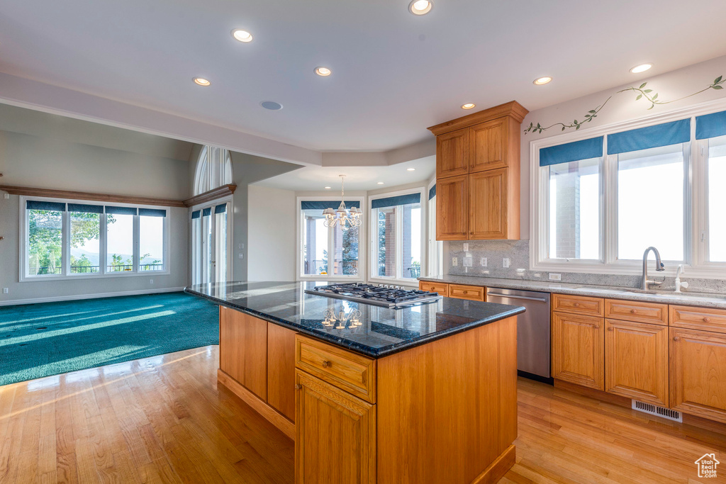 Kitchen featuring dark stone counters, tasteful backsplash, a kitchen island, appliances with stainless steel finishes, and light hardwood / wood-style floors