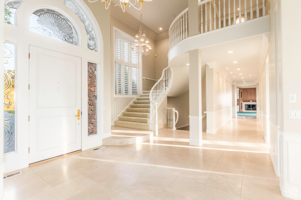 Tiled entryway featuring ornamental molding, a notable chandelier, and a towering ceiling