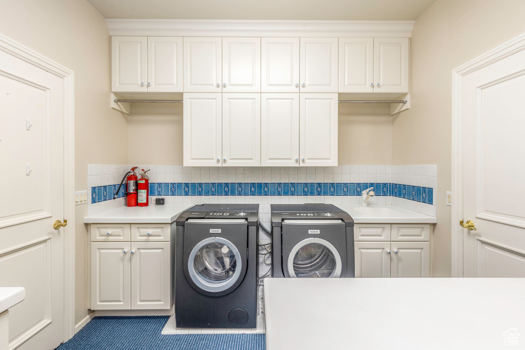 Clothes washing area with separate washer and dryer, dark tile patterned flooring, cabinets, and sink