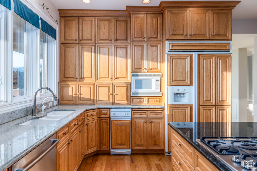 Kitchen with light wood-type flooring, light stone counters, stainless steel appliances, and sink