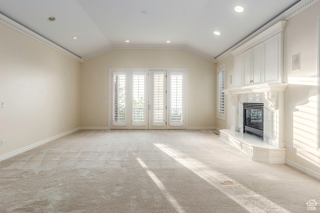 Unfurnished living room featuring ornamental molding, vaulted ceiling, light carpet, and a fireplace