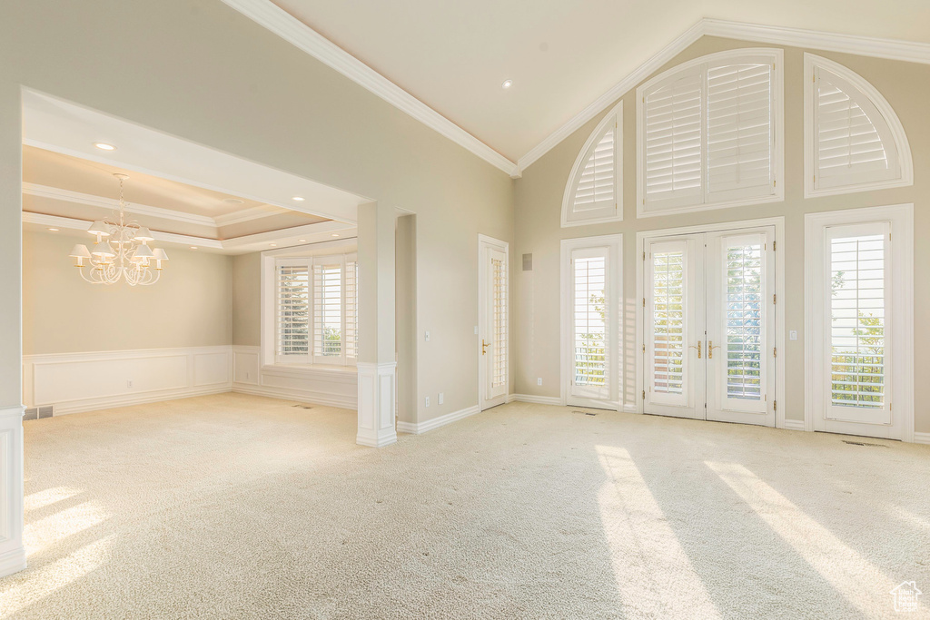 Empty room featuring a raised ceiling, an inviting chandelier, light carpet, crown molding, and a high ceiling