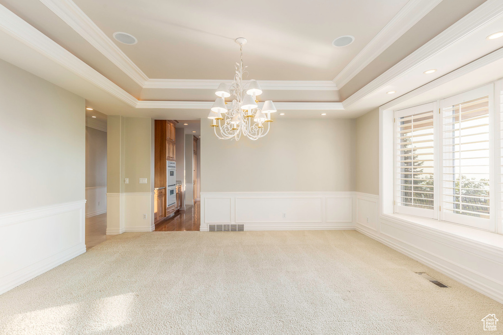 Spare room with a raised ceiling, carpet, ornamental molding, and a chandelier