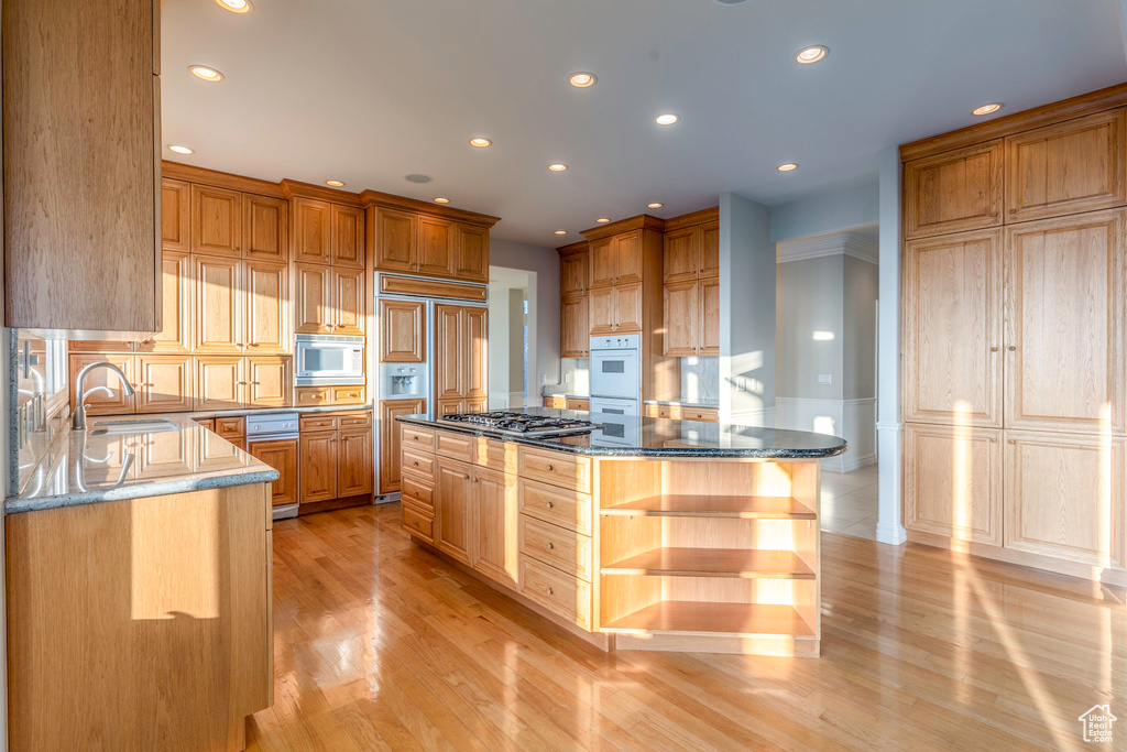 Kitchen featuring dark stone countertops, built in appliances, a kitchen island, sink, and light hardwood / wood-style floors