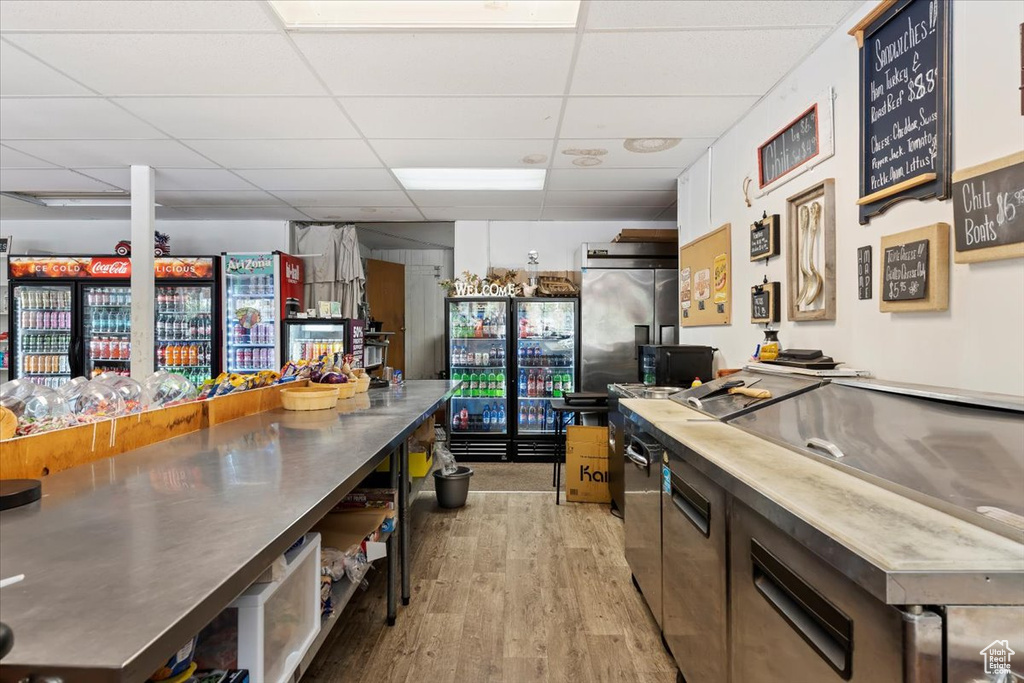 Kitchen with a drop ceiling, light hardwood / wood-style flooring, high quality fridge, and stainless steel counters