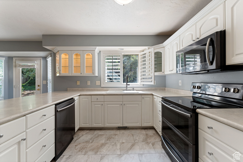 Kitchen featuring dishwashing machine, range with two ovens, white cabinets, sink, and light tile patterned floors