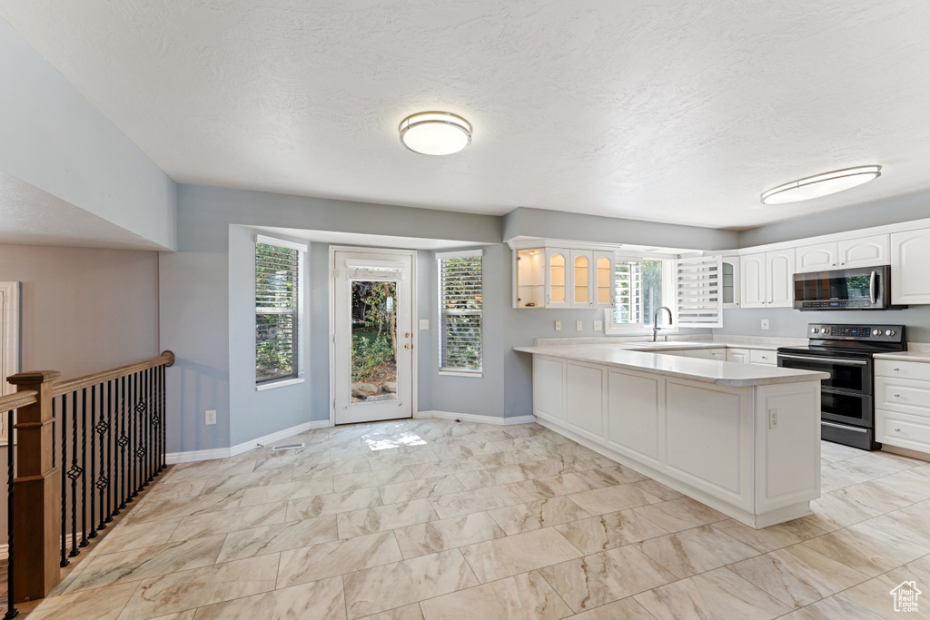 Kitchen featuring stainless steel appliances, white cabinets, sink, kitchen peninsula, and light tile patterned flooring