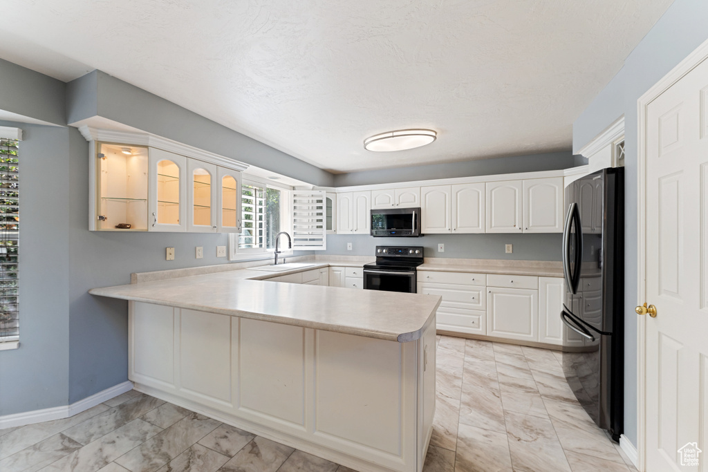 Kitchen with electric range oven, kitchen peninsula, refrigerator, light tile patterned flooring, and white cabinetry