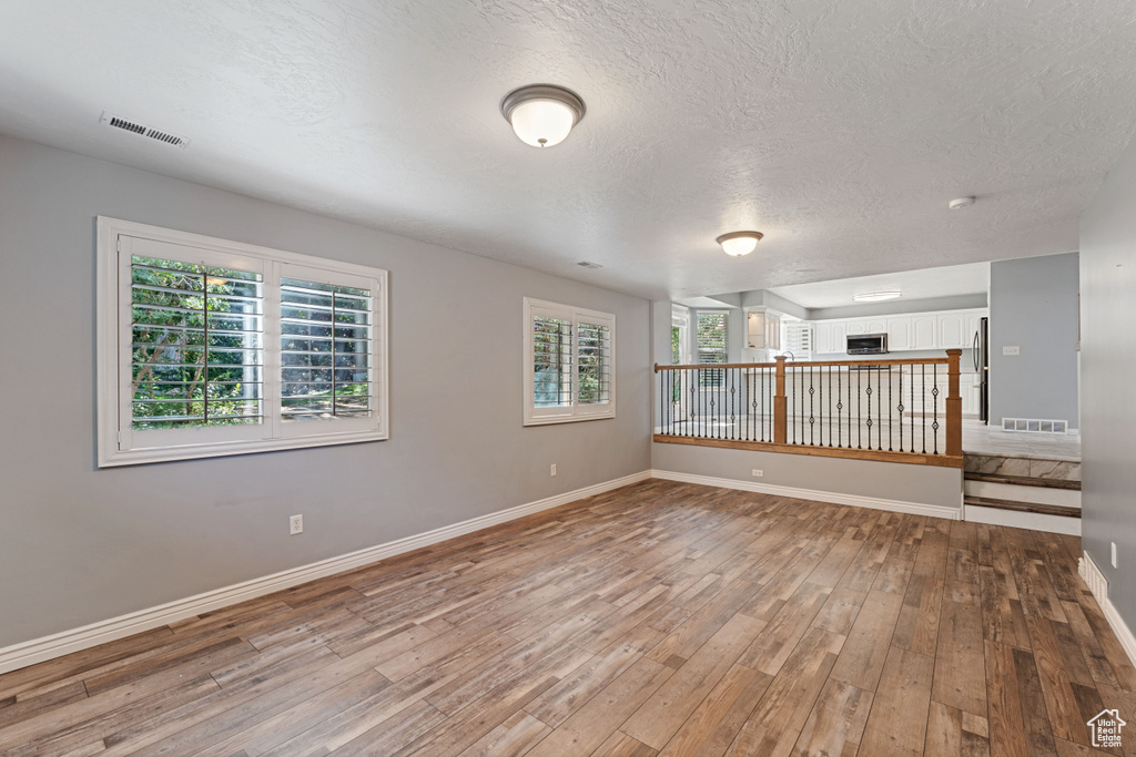 Spare room featuring light wood-type flooring, a healthy amount of sunlight, and a textured ceiling