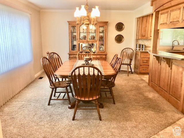 Carpeted dining space with ornamental molding, sink, and a chandelier