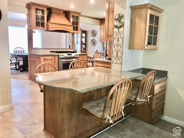 Kitchen featuring custom exhaust hood, stainless steel range oven, kitchen peninsula, and tile patterned flooring