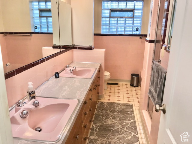 Bathroom with tile patterned floors, tile walls, double vanity, and toilet