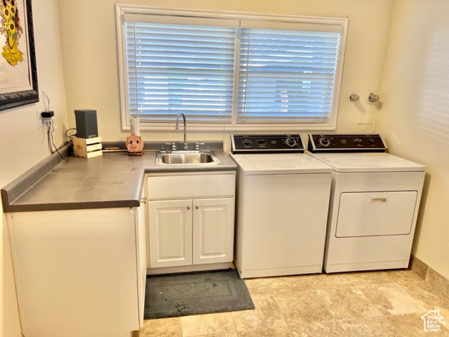 Clothes washing area with cabinets, light tile patterned floors, sink, and washer and clothes dryer