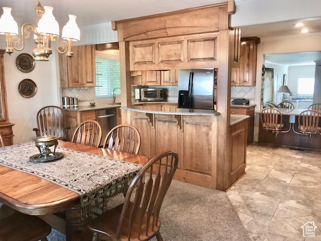 Kitchen with appliances with stainless steel finishes, pendant lighting, decorative backsplash, light tile patterned flooring, and a chandelier