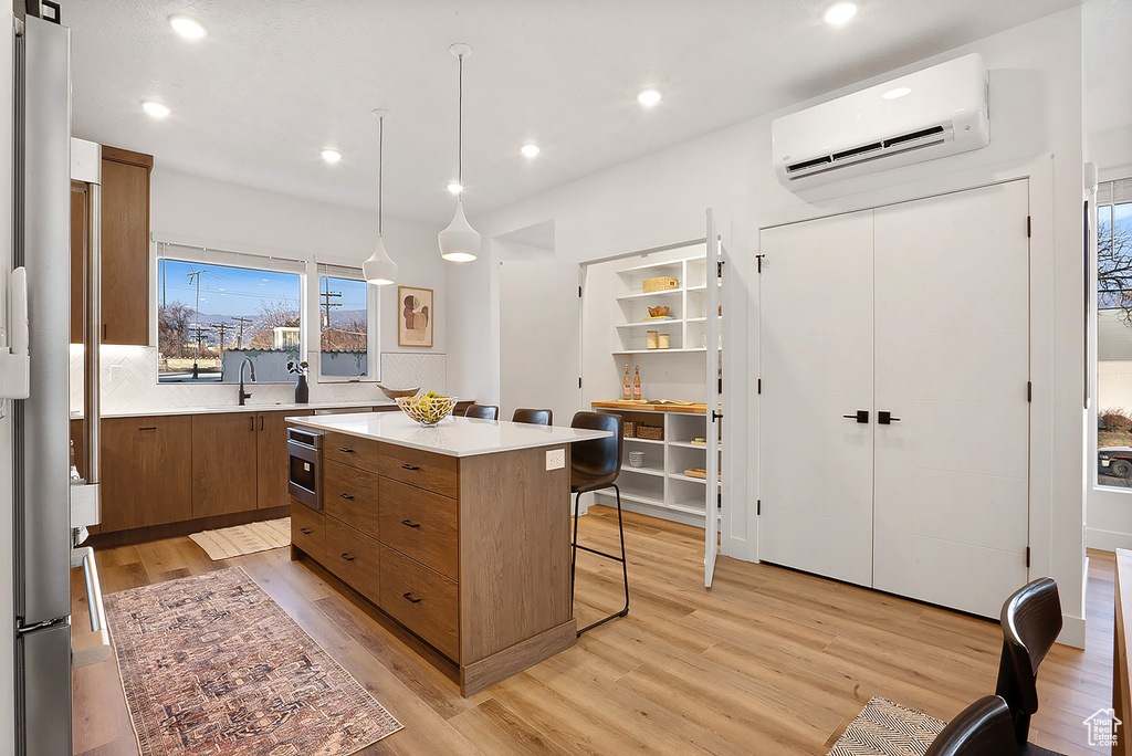 Kitchen featuring a wall unit AC, a breakfast bar, wall oven, light hardwood / wood-style floors, and a kitchen island