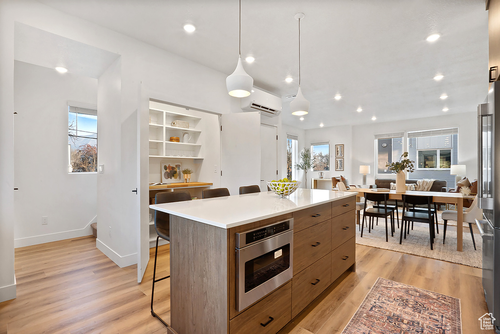 Kitchen featuring a wall mounted air conditioner, a center island, light wood-type flooring, and stainless steel appliances