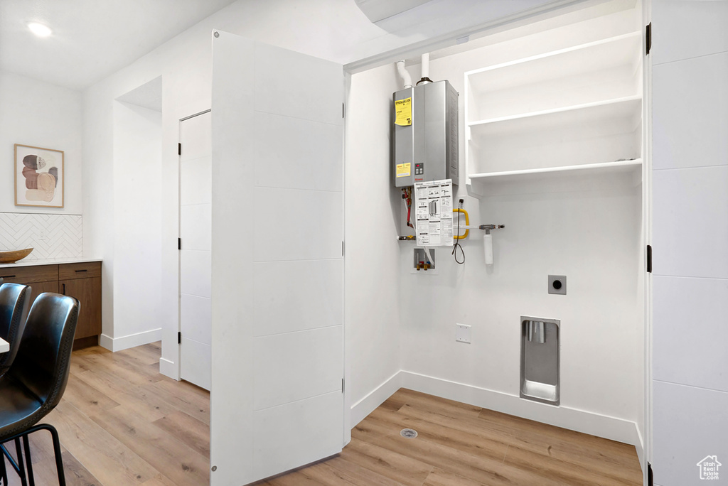 Clothes washing area featuring tankless water heater, hookup for an electric dryer, and light hardwood / wood-style floors