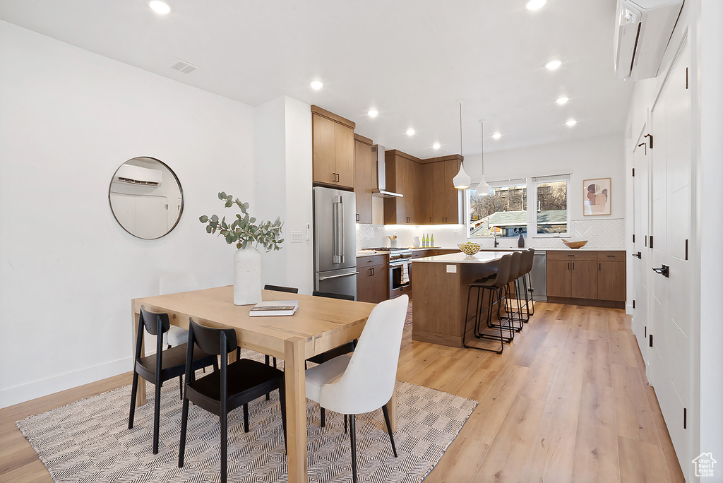 Dining area with a wall mounted air conditioner and light wood-type flooring