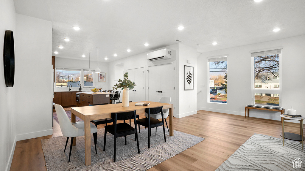 Dining space featuring a wall mounted air conditioner, light hardwood / wood-style flooring, and plenty of natural light