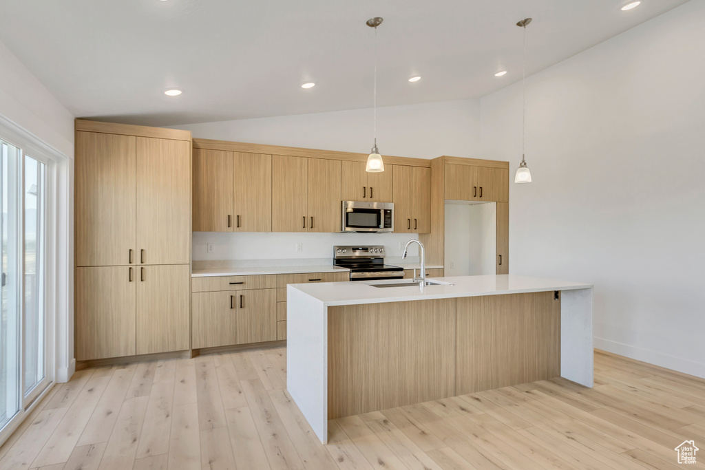 Kitchen with appliances with stainless steel finishes, light brown cabinetry, vaulted ceiling, light hardwood / wood-style flooring, and a center island with sink