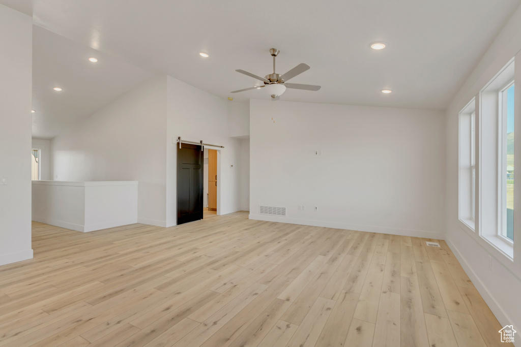 Unfurnished room featuring a barn door, high vaulted ceiling, light hardwood / wood-style floors, and ceiling fan