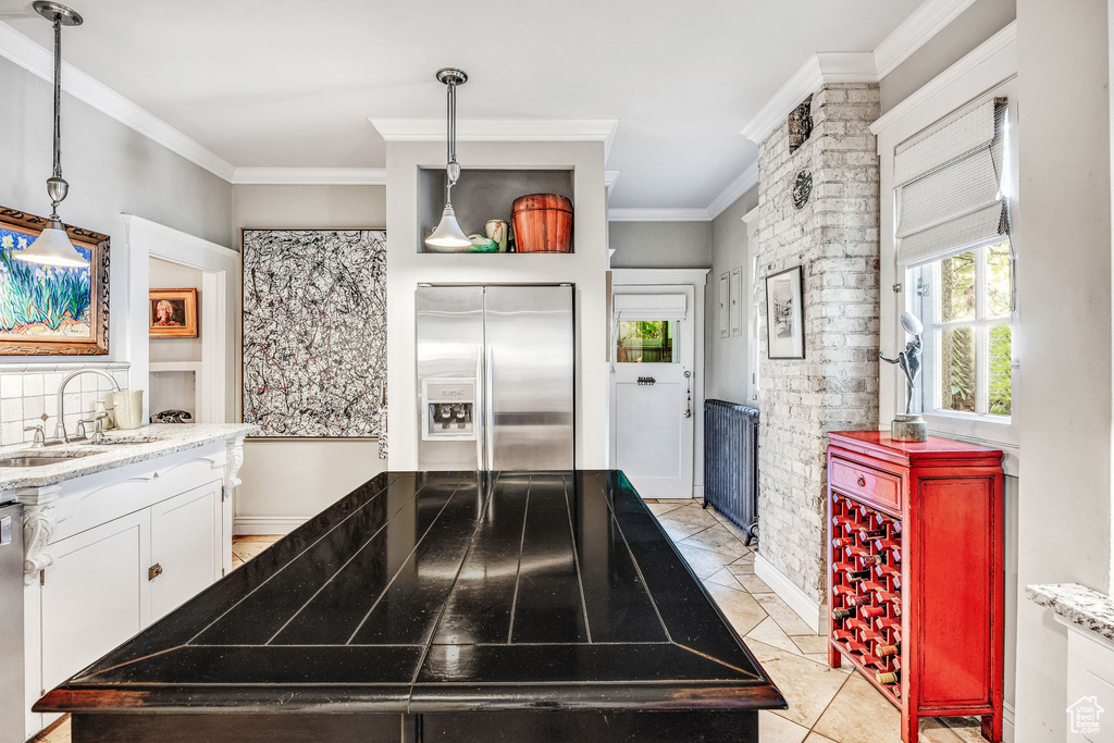 Kitchen featuring sink, hanging light fixtures, light tile patterned floors, stainless steel refrigerator with ice dispenser, and white cabinetry