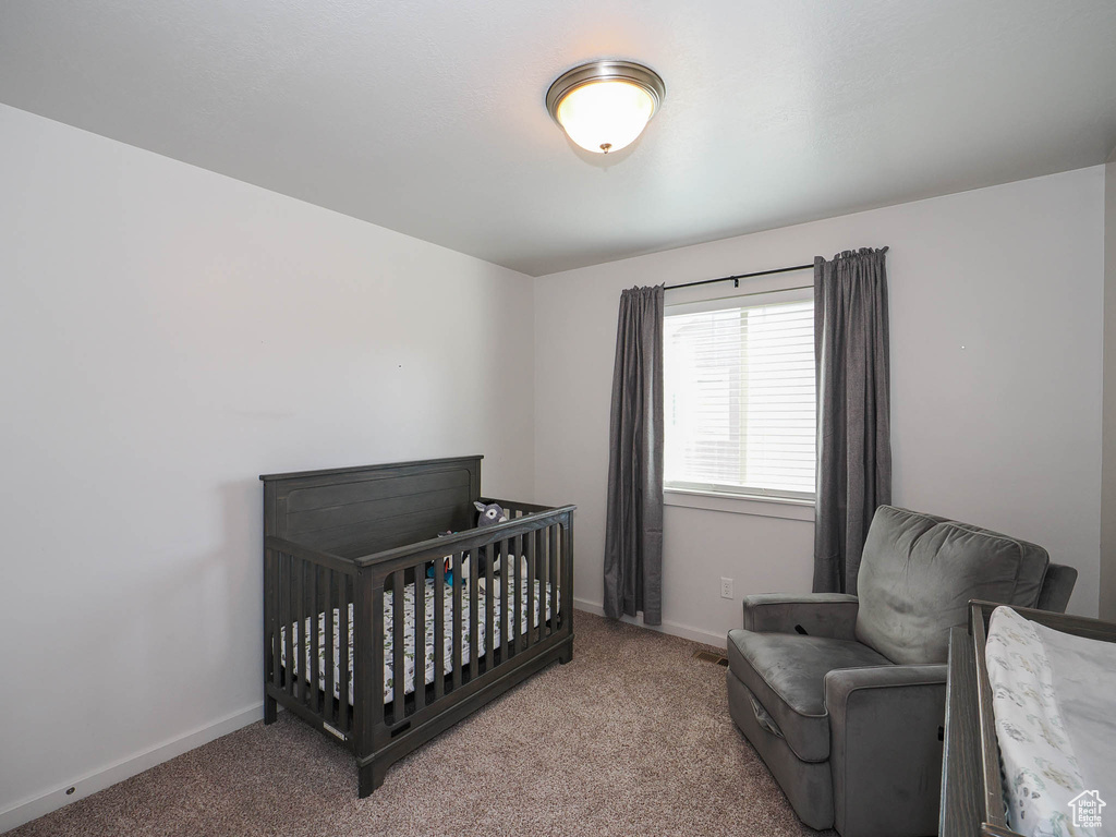 Bedroom featuring a nursery area and light colored carpet