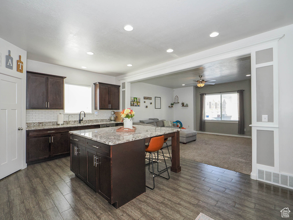 Kitchen featuring a breakfast bar area, tasteful backsplash, a center island, dark colored carpet, and ceiling fan