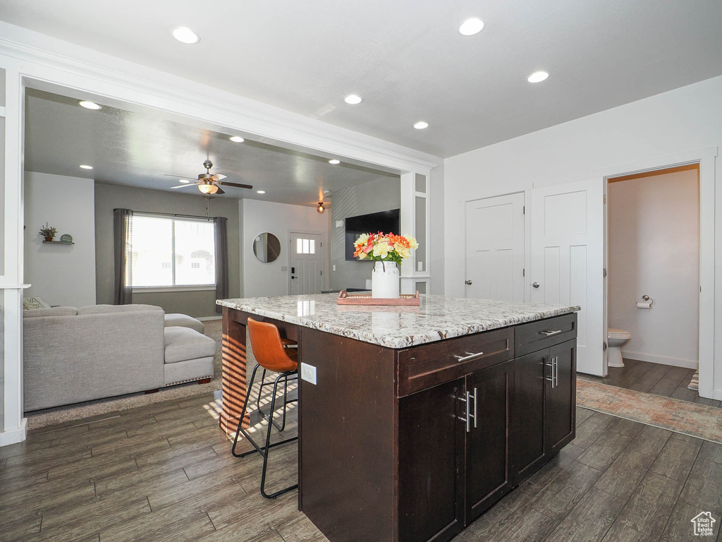 Kitchen with a breakfast bar, dark brown cabinets, dark wood-type flooring, a kitchen island, and ceiling fan