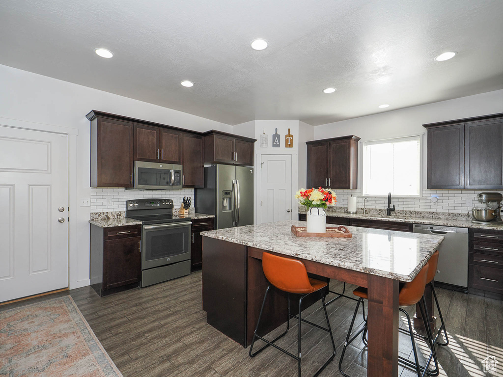 Kitchen with appliances with stainless steel finishes, a kitchen island, decorative backsplash, a kitchen breakfast bar, and dark hardwood / wood-style flooring