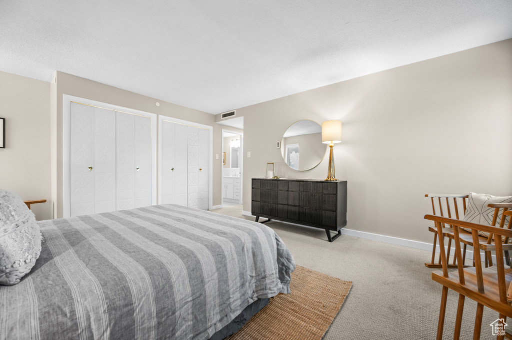 Bedroom with multiple closets, light colored carpet, and ensuite bathroom