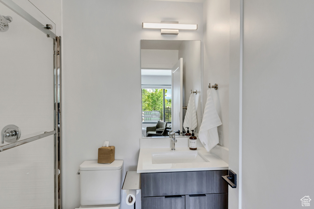 Bathroom featuring a shower with shower door, vanity, and toilet