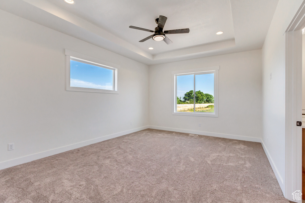 Carpeted empty room with ceiling fan and a raised ceiling