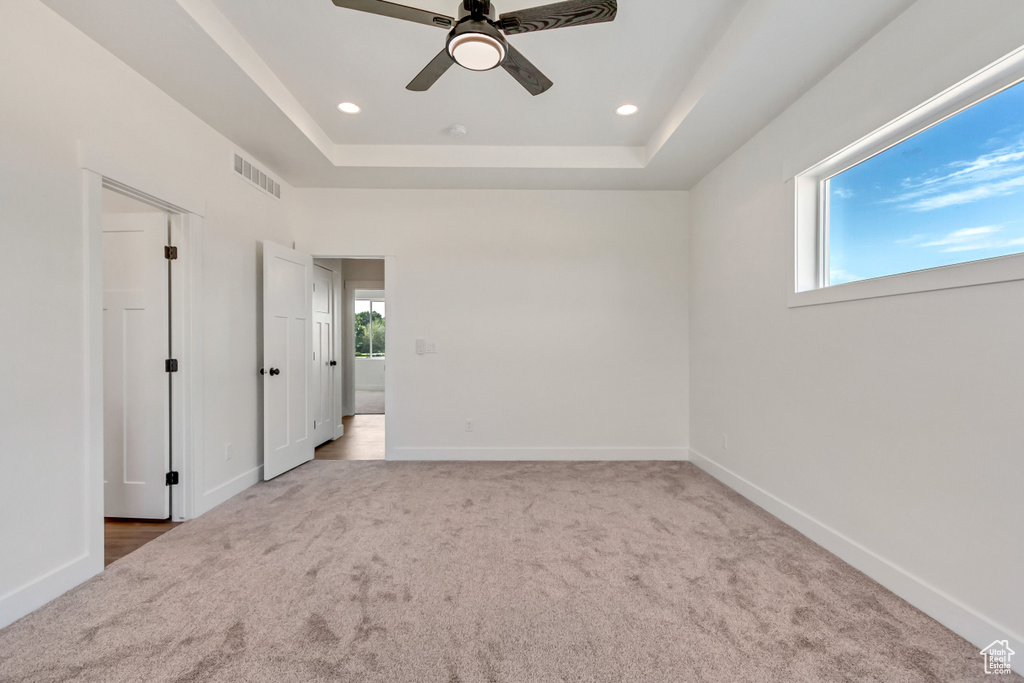 Unfurnished bedroom featuring light carpet, a raised ceiling, and ceiling fan