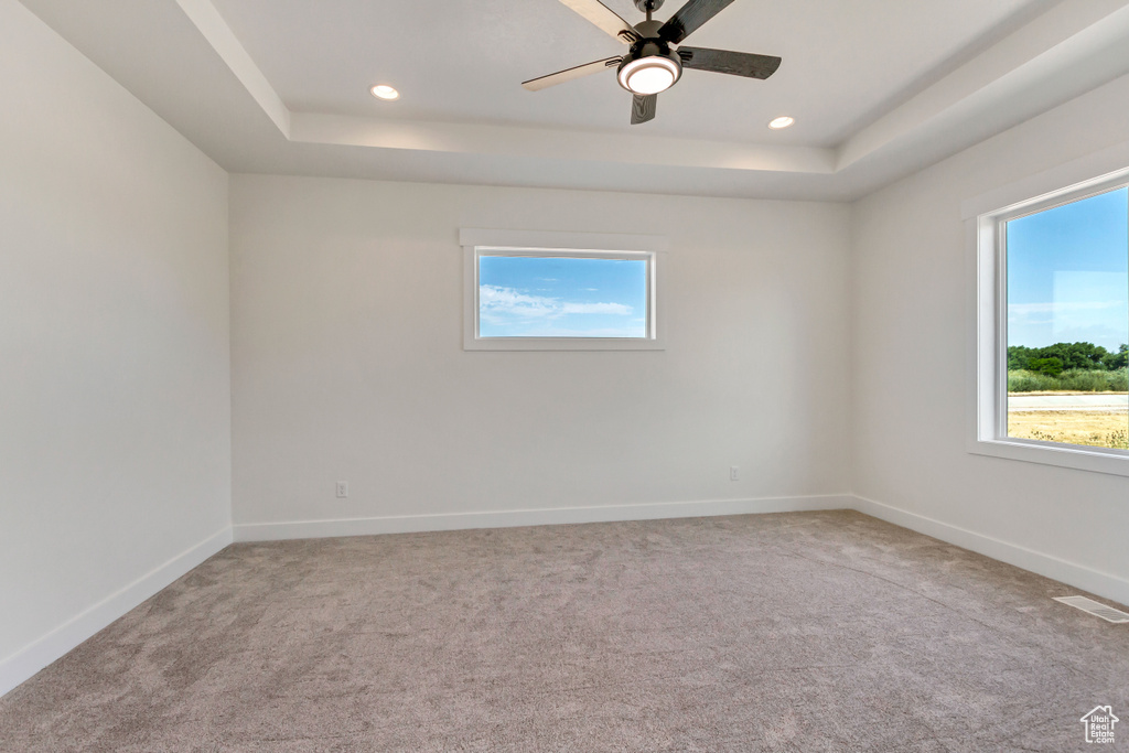 Carpeted empty room featuring a tray ceiling and ceiling fan