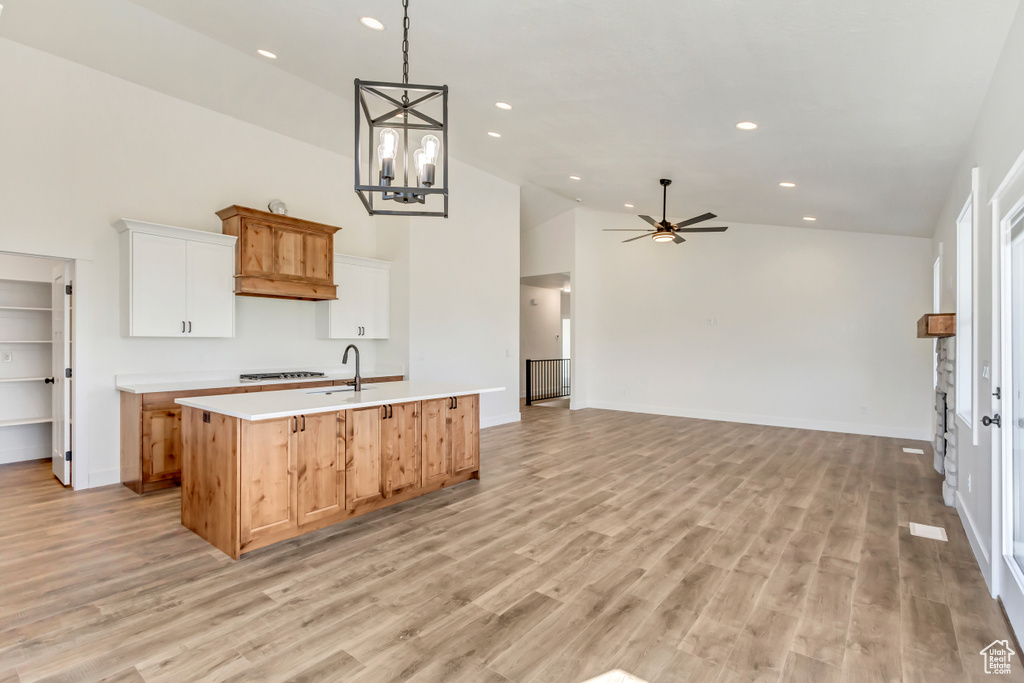 Kitchen featuring white cabinetry, light hardwood / wood-style flooring, ceiling fan with notable chandelier, an island with sink, and high vaulted ceiling