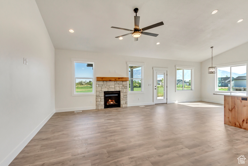 Unfurnished living room featuring a stone fireplace, lofted ceiling, light wood-type flooring, and ceiling fan