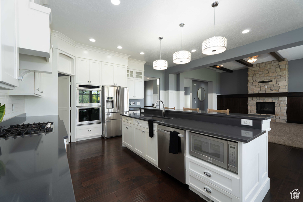 Kitchen with appliances with stainless steel finishes, white cabinetry, and a stone fireplace