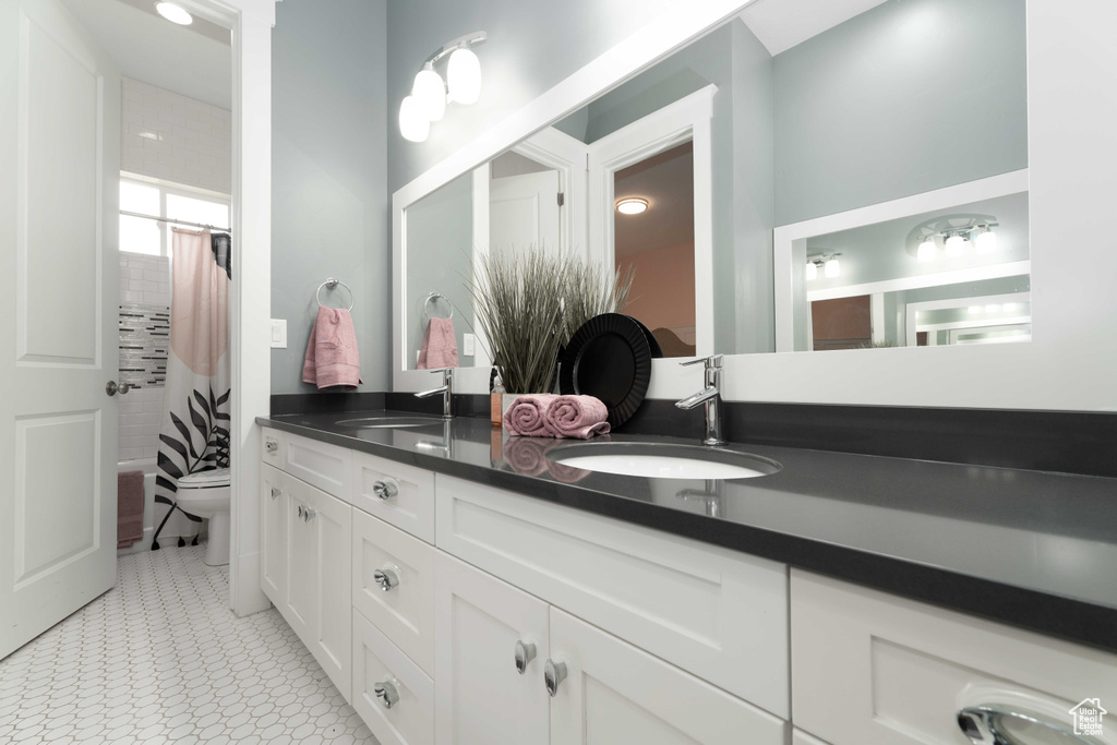 Full bathroom featuring toilet, tile patterned floors, double sink vanity, and shower / bath combination with curtain
